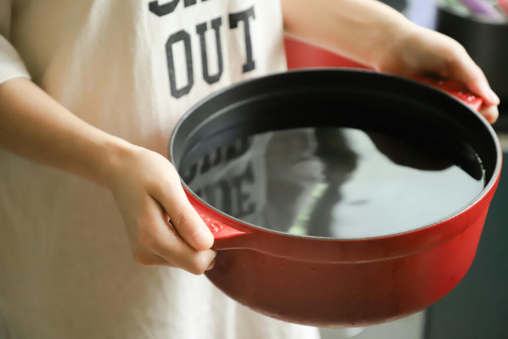 Close-up of hands holding a red pot filled with water, indoors.