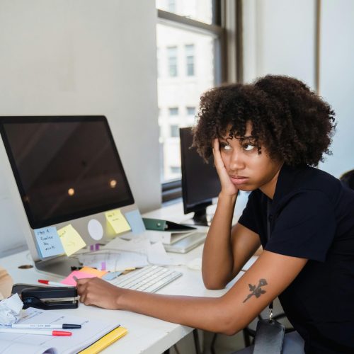 pexels photo 12911184 12911184 Woman with afro hairstyle looks frustrated at her office desk filled with notes.