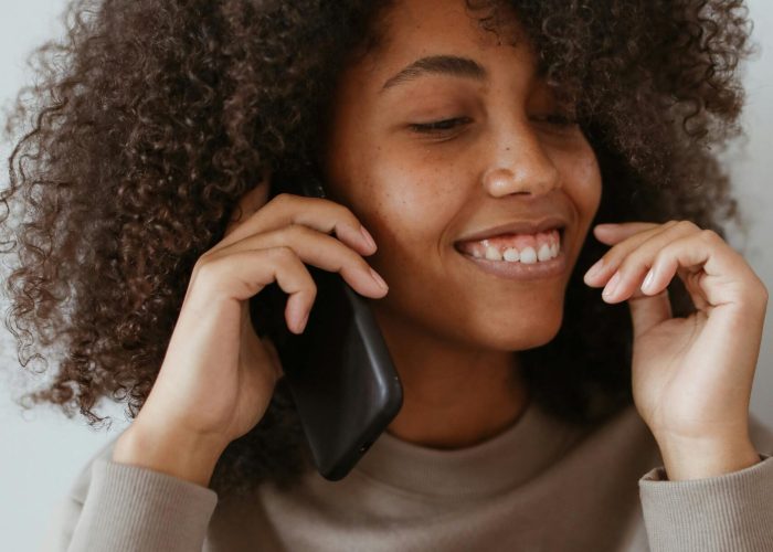 Smiling woman with afro hair enjoying a phone call indoors, wearing a casual sweater.